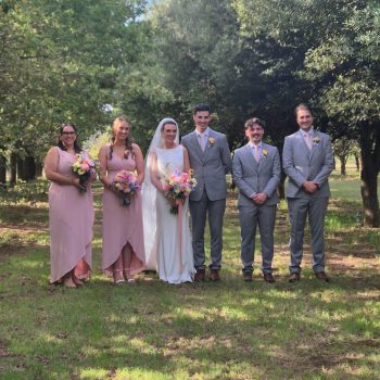 Bridal party gathered around the wedding couple smiling for a group photo.