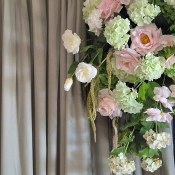 Asymmetrical floral arrangement of roses and greenery cascading down a sage green curtain.