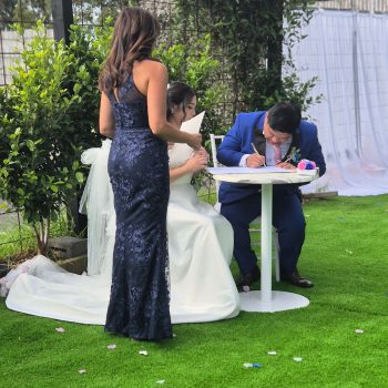 Groom signing official marriage documents at the ceremony table.
