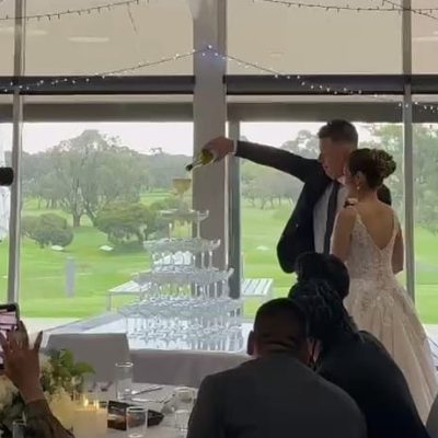 Joel and Narin pouring champagne into a stacked champagne tower during their wedding celebration.