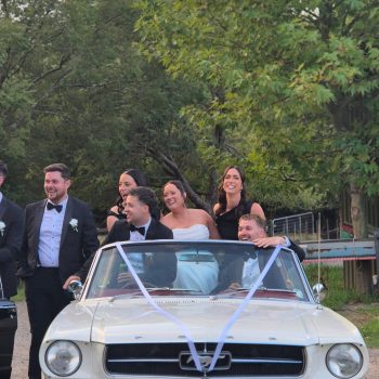 Couple and wedding party posing with car outdoors