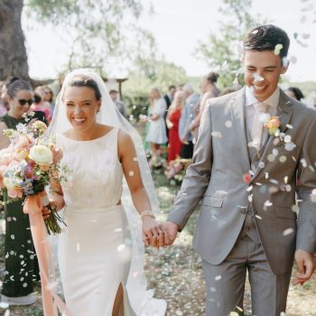 Couple walking through confetti as guests celebrate their wedding exit.