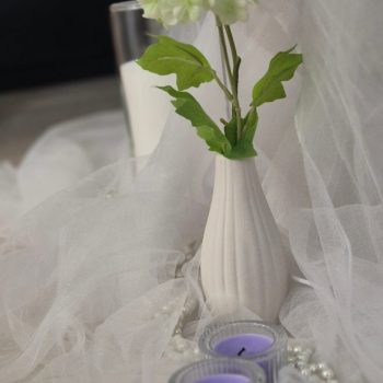 Purple tea light candles in glass holders surrounded by shimmering white pearl strands on a clear table.