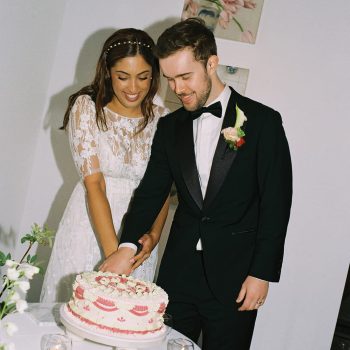 Couple cutting wedding cake together surrounded by guests at a joyful wedding reception