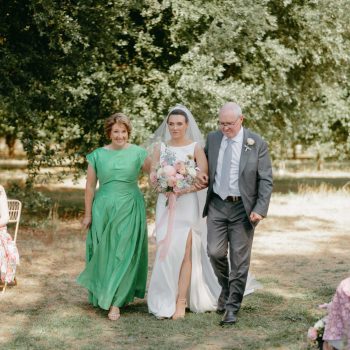 Bride walking down the aisle with both parents during an emotional ceremony moment.
