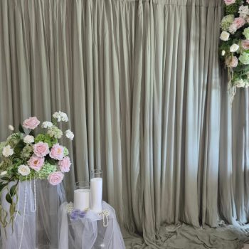 A sage green backdrop featuring blush pink roses and white tulle pedestal accents for a bridal shower.
