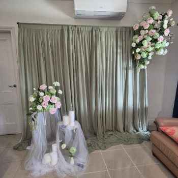 Floor-to-ceiling sage green curtains with a large asymmetrical floral arrangement of pink and white roses